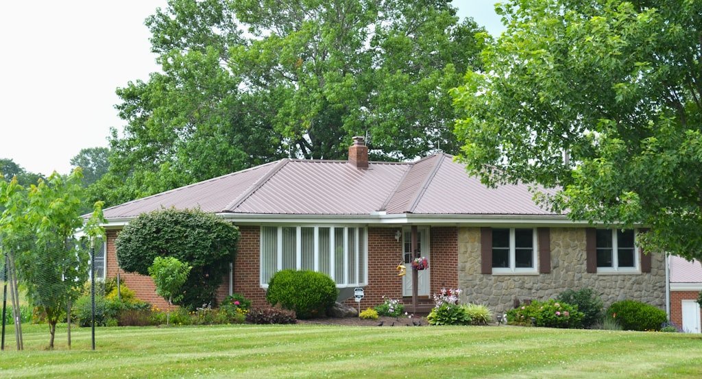 A single-storey brick and stone home with a metal roof and established landscaping.